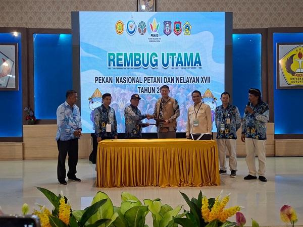 Panelis berdiri di depan spanduk “Rembug Utama” di aula dengan meja berlapis kain kuning.