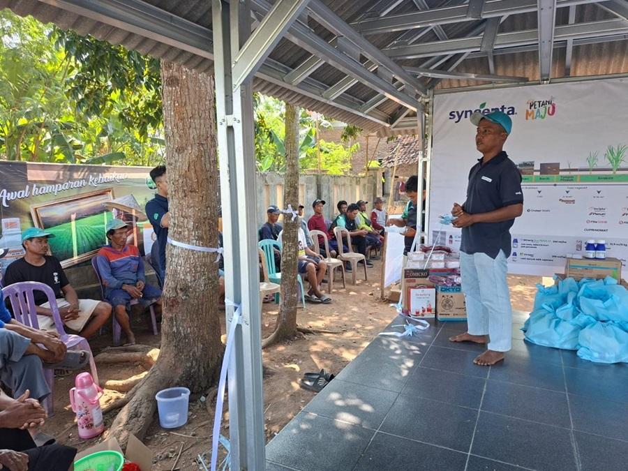 Pria berbicara di panggung kecil, audiens duduk di bawah atap terbuka.