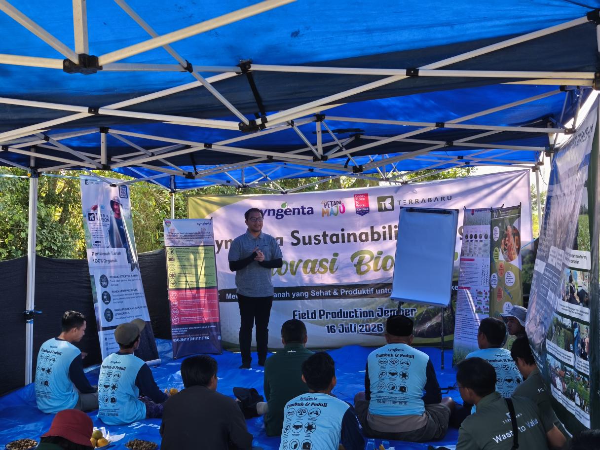 Presentasi di bawah tenda biru, audiens duduk mendengarkan di depan panggung.