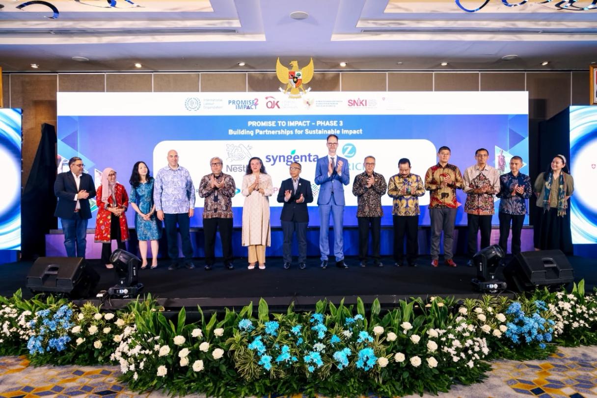 Foto bersama para pejabat dan peserta di panggung acara, dekorasi bunga di depan.
